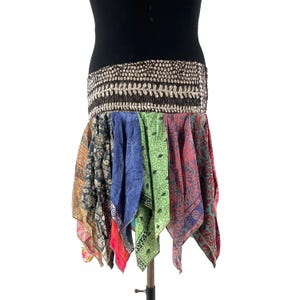 May include: A colorful, patchwork skirt with a wide, embellished waistband. The skirt features panels of patterned fabric in various colors, including blue, green, red, and orange. The waistband is a dark brown with a decorative, silver-toned trim.