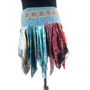 May include: A colorful, patchwork skirt with a blue elastic waistband. The skirt features panels of various patterned fabrics in shades of blue, red, and silver. The skirt has a unique, asymmetrical hemline.