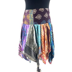 Puede incluir: Una falda patchwork con una variedad de paneles de tela coloridos. La falda presenta una cintura ancha y elástica con una mezcla de patrones y colores, incluyendo morado, dorado y cachemira. El dobladillo de la falda es asimétrico.