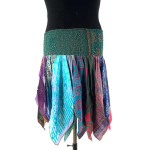 May include: A colorful, patchwork skirt with a green elastic waistband. The skirt features various patterned fabrics in shades of blue, purple, pink, and green. The skirt is displayed on a black mannequin.