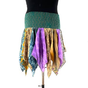Könnte beinhalten: Ein farbenfroher, im Bohème-Stil gehaltener Rock mit einem grünen, elastischen Bund. Der Rock besteht aus Stoffbahnen mit verschiedenen Mustern in Blau-, Gold-, Lila- und Beigetönen. Der Rock hat einen Taschentuchsaum, der eine einzigartige, fließende Silhouette erzeugt.