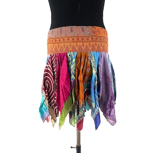 Op de afbeelding: Een kleurrijke patchwork rok met een oranje elastische tailleband. De rok heeft verschillende stoffen met patronen in roze, blauw, paars en groen. De rok wordt op een mannequin getoond.