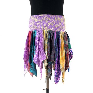 May include: A patchwork skirt with a wide, elasticated waistband. The skirt is made from various patterned silk fabrics in shades of purple, teal, yellow, and red. The skirt is designed to be worn at the waist and has a flowing, asymmetrical hemline.