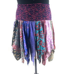 May include: A colorful patchwork skirt with a dark blue, patterned elastic waistband. The skirt features a variety of patterned fabrics in shades of black, red, teal, purple, and pink. The skirt is displayed on a mannequin.
