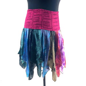 May include: A colorful, layered skirt with a wide, elasticized magenta waistband. The skirt features panels of various patterned fabrics in shades of blue, green, purple, and brown. The skirt is designed to be worn at the waist.