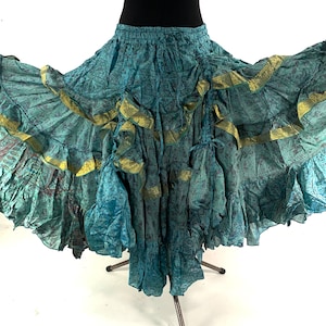 Puede incluir: Falda de color turquesa con un diseño fluido y en capas. La falda presenta un estampado floral y ribetes dorados a lo largo de los volantes. Se frunce en la cintura y tiene una silueta amplia y acampanada, adecuada para la danza o estilos bohemios.