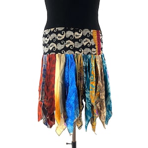 May include: A vibrant, bohemian skirt with a black elasticated waistband adorned with a paisley design. The skirt is constructed from panels of fabric in red, blue, yellow, and brown. The skirt is displayed on a stand against a white backdrop.