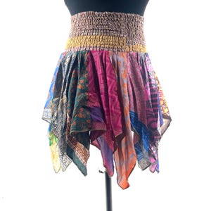 May include: A patchwork skirt with a wide, elasticated waistband. The skirt is made from panels of patterned fabrics in shades of blue, pink, green, and orange. It has an asymmetrical hemline and is displayed on a mannequin.