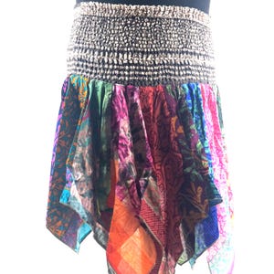 May include: A vibrant, asymmetrical skirt with a patterned design. The skirt has a wide, elasticated waistband in a neutral tone. The lower section is made of various fabric panels in shades of pink, green, orange, and blue.