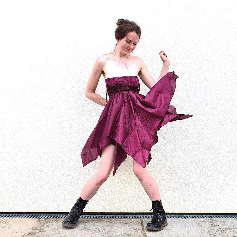 May include: A woman wearing a strapless, burgundy, asymmetrical dress with a flowing skirt. She is wearing black boots and has her hair pulled back in a bun.