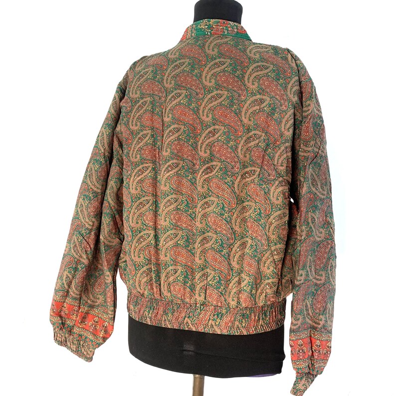 May include: A green and brown paisley patterned bomber jacket with a ribbed waistband and cuffs.