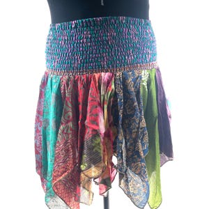 May include: A patchwork mini skirt with a smocked waistband. The skirt is made from panels of patterned fabrics in teal, red, blue, green, and purple. The skirt has an asymmetrical hemline, creating a flowing, bohemian style. The waist is approximately 60 cm.