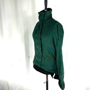 May include: A dark green corduroy jacket with a high collar and gold buttons. The jacket has a long, pointed back hem and a decorative trim on the pockets.