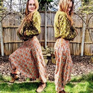 May include: A woman wearing a green patterned jacket and matching pants with a paisley print. The pants are loose fitting and have a wide leg.
