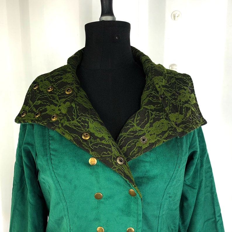 May include: A green corduroy jacket with a double breasted closure and a black lace collar with gold accents.