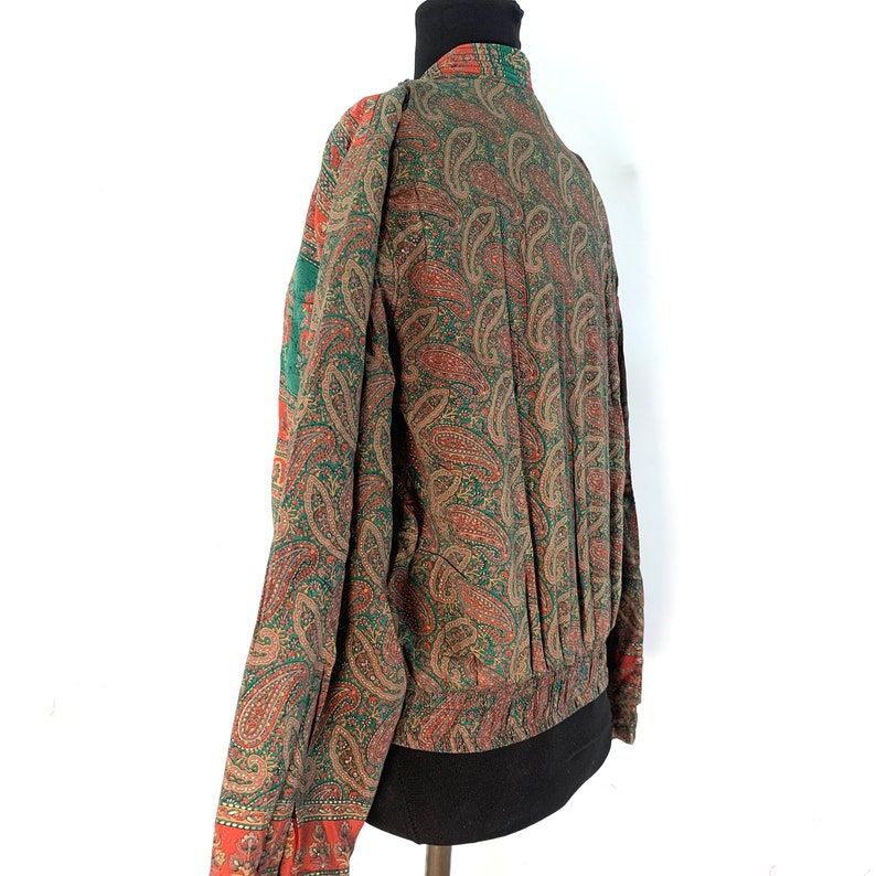 May include: A green and orange paisley patterned jacket with a long sleeve and a gathered elastic waistband.