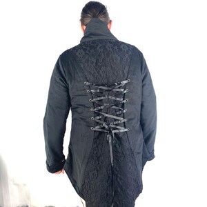 May include: Black long-sleeved jacket with a lace back and a corset-style lacing detail. The jacket has a high collar and a long, flowing tail.