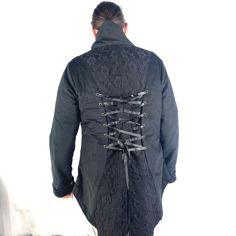 May include: Black long-sleeved jacket with a lace back and a corset-style lacing detail. The jacket has a high collar and a long, flowing tail.