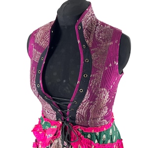 May include: A sleeveless vest in shades of purple and gold, featuring a high collar and a lace-up front. The vest has a quilted texture and is adorned with metallic gold accents. The bottom of the vest is connected to a skirt with pink and green fabric.