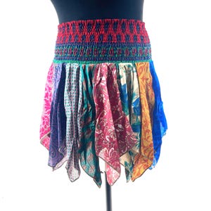 May include: A colorful, patchwork skirt with a red, elasticized waistband. The skirt features panels of various patterned fabrics in shades of pink, purple, teal, burgundy, blue, and yellow. The skirt is designed to be worn at the waist.