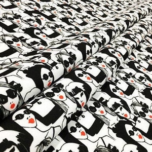 May include: White fabric with a repeating pattern of stylized faces in black and white. Each face has sunglasses and red lips. The fabric is folded, showing the pattern's repeating design.