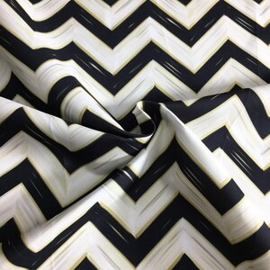 May include: Close-up of a fabric with a black, white, and gold chevron pattern. The fabric is folded, showing the texture and design. The zig-zag pattern is bold and graphic, creating a modern aesthetic.