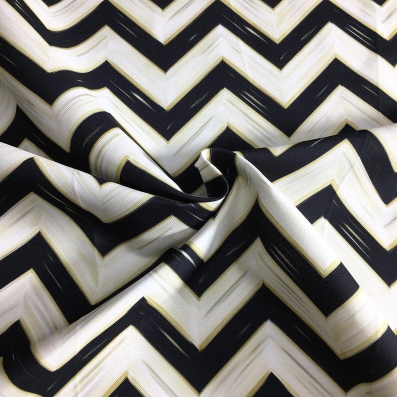 May include: Close-up of a fabric with a black, white, and gold chevron pattern. The fabric is folded, showing the texture and design. The zig-zag pattern is bold and graphic, creating a modern aesthetic.
