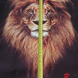 May include: A black fabric panel featuring a detailed, realistic lion head print in shades of brown, gold, and tan. A yellow measuring tape is placed vertically over the lion's face, showing a measurement of approximately 32 centimetres in length.