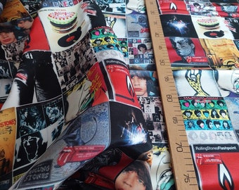 May include: Fabric featuring a collage of Rolling Stones album covers and band member portraits. The design includes red, black, white, and yellow elements. A wooden ruler with inch markings is visible on the right side of the fabric.