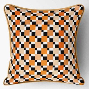 K&ouml;nnte beinhalten: Quadratisches Zierkissen mit einem geometrischen Muster aus orangefarbenen, schwarzen, wei&szlig;en und beigefarbenen Quadraten. Das Kissen hat einen beigen Rand und eine quadratische Form. Es wird wahrscheinlich f&uuml;r die Heimdekoration verwendet.