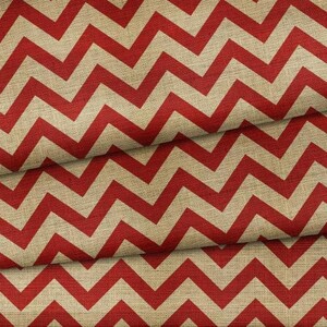 May include: Red and beige chevron pattern fabric. The fabric has a textured appearance, with a repeating zigzag design in red against a beige background. The fabric is folded, showing the pattern's continuity.