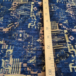 May include: A dark blue fabric featuring a repeating geometric pattern in shades of gold and light brown. A wooden ruler is placed vertically against the textile, showing measurement markings from 40 cm to 80 cm along its straight edge.