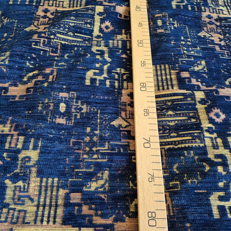 May include: A dark blue fabric featuring a repeating geometric pattern in shades of gold and light brown. A wooden ruler is placed vertically against the textile, showing measurement markings from 40 cm to 80 cm along its straight edge.