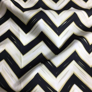 May include: Close-up of a fabric with a bold chevron pattern. The design features alternating black and white zigzags, with gold brushstroke accents. The fabric has a slightly textured appearance, with soft folds.