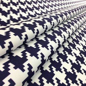 Può includere: Primo piano di un tessuto piegato con un classico motivo a pied-de-poule. Il tessuto presenta un design ripetuto di forme blu navy su sfondo bianco. Il materiale sembra essere un tessuto di peso medio.