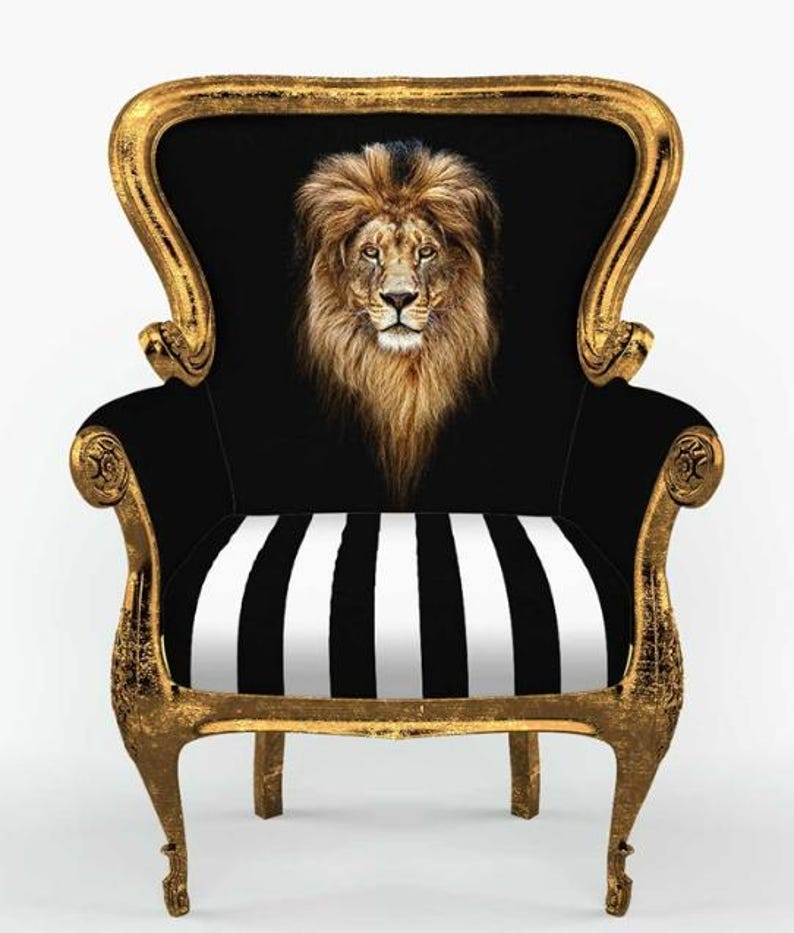 May include: An armchair with a distressed gold frame and black upholstery. The backrest features a detailed, centred portrait of a lion's head with a full mane. The seat cushion displays a bold, vertical black and white striped pattern.