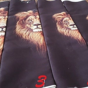 May include: Four rectangular fabric panels featuring a printed lion head design on a dark brown background. The panels are arranged side by side, each labelled with a red number from one to four, showing varying scales of the lion's face.