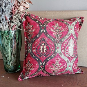 May include: A red and green patterned throw pillow with a floral design. The pillow is made of a soft, textured fabric and has a square shape.