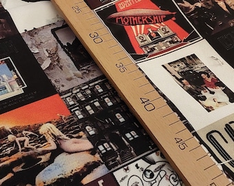 May include: Fabric featuring a collage of Led Zeppelin album covers, including "Mothership" with a red airship design. The fabric has a variety of album art in a patchwork style, with a wooden ruler laid across the fabric.