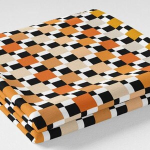 K&ouml;nnte beinhalten: Gefalteter Stoff mit einem sich wiederholenden Schachbrettmuster in Schwarz, Wei&szlig;, Orange und Beige. Der Stoff ist sauber gefaltet und zeigt das Design. Das Farbschema erzeugt eine Retro-Atmosph&auml;re.