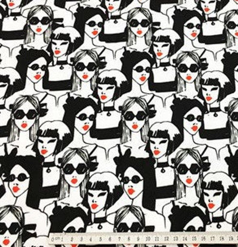 May include: Black and white fabric featuring a repeating pattern of stylized women's faces. Each woman wears sunglasses and has red lipstick. The women are dressed in black and white outfits. A ruler is at the bottom of the image.