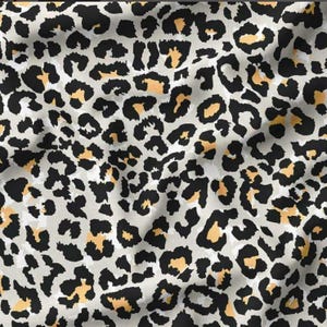 May include: Close-up of a fabric with a leopard print pattern. The design features black spots with orange-yellow centres on a light grey background. The fabric has a soft, flowing appearance.