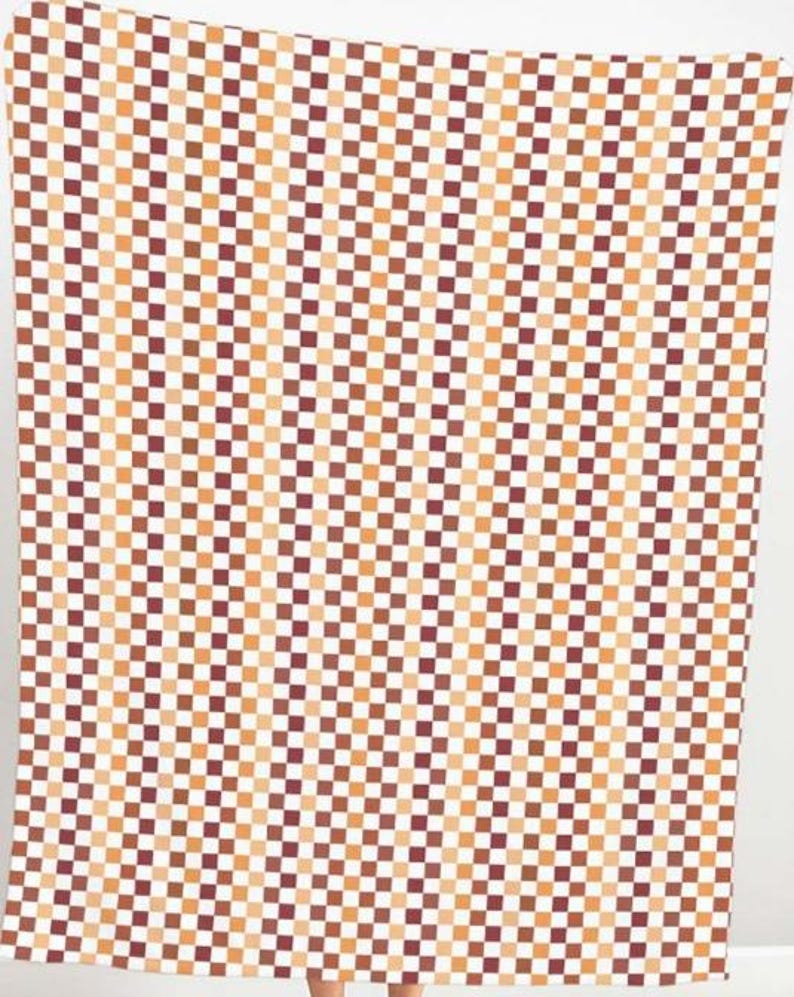 K&ouml;nnte beinhalten: Ein gro&szlig;es, rechteckiges Textil mit einem sich wiederholenden Schachbrettmuster. Die Quadrate wechseln sich in Braun-, Orange- und Wei&szlig;t&ouml;nen ab. Das Textil h&auml;ngt und das Muster ist &uuml;ber die gesamte Oberfl&auml;che sichtbar.