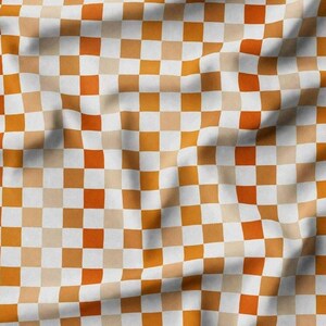 K&ouml;nnte beinhalten: Ein Stoff mit einem karierten Muster in Orange-, Wei&szlig;- und Beiget&ouml;nen. Die Quadrate sind in einem Raster angeordnet und erzeugen ein ansprechendes Design. Der Stoff wirkt weich und flie&szlig;end, mit sanften Falten und Schatten.