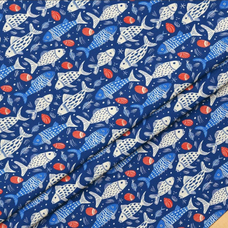 May include: A navy blue fabric with a repeating pattern of stylized fish in white and blue, along with red seashell-like shapes and small star-like elements. The fabric is folded, showing the pattern at different angles.