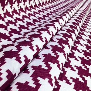 May include: White and burgundy fabric with a houndstooth pattern. The fabric is folded and has a textured surface.