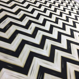 May include: A fabric with a repeating black and white chevron pattern. The design features thick, zig-zag lines in black against a white background, with subtle gold accents. The fabric has a textured appearance.