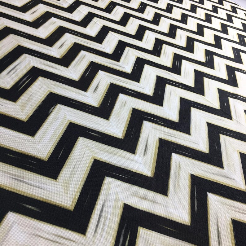 May include: A fabric with a repeating black and white chevron pattern. The design features thick, zig-zag lines in black against a white background, with subtle gold accents. The fabric has a textured appearance.