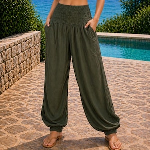 May include: A white sleeveless wrap-style crop top with thin halter straps paired with olive green high-waisted loose-fitting trousers featuring a wide smocked elastic waistband, side pockets, and gathered elastic cuffs at the ankles.