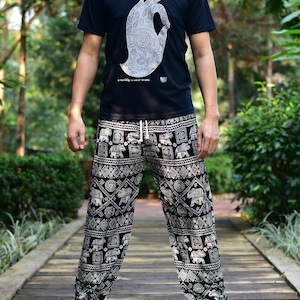 May include: A person wearing a black t-shirt with a white hand graphic and patterned black and white pants. The pants have an elephant and geometric design. The t-shirt has the text "A world in the palm of the hand".